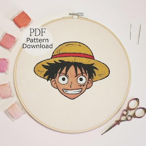 Puede incluir: Aro de bordado bordado con un personaje de dibujos animados con un sombrero de paja. La cara del personaje está detallada con cabello negro, una cicatriz y una amplia sonrisa. El texto "PDF Pattern Download" es visible. También hay carretes de hilo rosa y naranja y tijeras de bordar.
