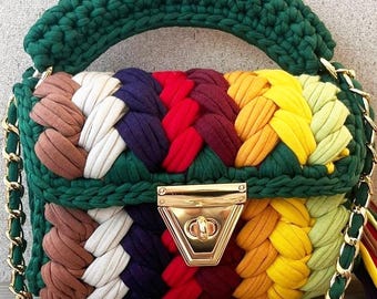 May include: A small, green crocheted handbag with a gold chain strap and a gold clasp. The bag is made with colorful yarn in shades of brown, white, purple, red, orange, and yellow.