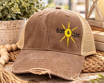 May include: A brown distressed baseball cap with a mesh back and a frayed brim. The front features an embroidered yellow sun graphic with the black text Salt & Light positioned across the center of the sun design.