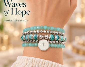 May include: A multi-strand beaded bracelet featuring light blue faceted beads, silver-toned metallic spheres, and teal patterned beads. A white circular charm with a small silver cross hangs from the center. Text reads Waves of Hope Warrior Collective Co.