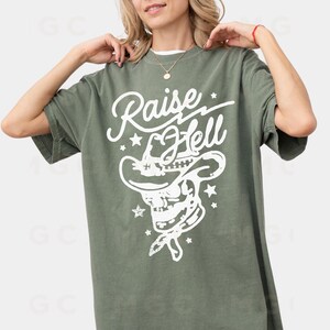 May include: A green t-shirt with a white graphic of a skull wearing a cowboy hat and the text "Raise Hell".
