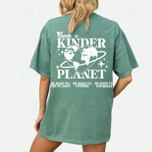 Peut inclure: Un t-shirt vert sarcelle avec un motif graphique blanc qui dit "Create a Kinder Planet" avec un globe en forme de c&oelig;ur et le texte "Be kind to the planet, Be kind to others, Be kind to yourself."