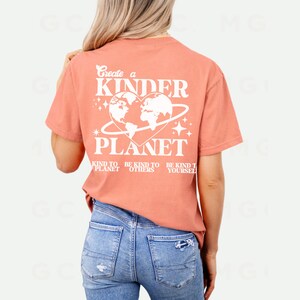 Peut inclure: Un t-shirt de couleur corail avec un motif blanc qui dit "Create a Kinder Planet" avec un globe en forme de c&oelig;ur et le texte "Be Kind to Planet, Be Kind to Others, Be Kind to Yourself".