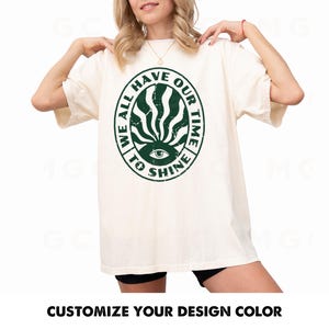 May include: A white t-shirt with a green circle graphic that says "We all have our time to shine".