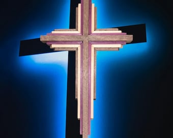 May include: A wooden cross with a layered design, featuring shades of gray, purple, and cream. The cross is set against a dark blue background with a subtle glow, creating a striking visual effect. The cross is a religious symbol.