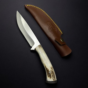 May include: A hunting knife with a white bone handle and a leather sheath. The sheath has decorative stitching and a brass button.