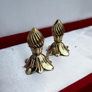Könnte beinhalten: Zwei goldene Kerzenhalter mit floralem Design. Die Kerzenhalter stehen auf einer weißen Oberfläche mit rotem Rand.
