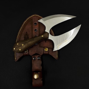 Op de afbeelding: Een op maat gemaakt mes met dubbele rand, met een donkerhouten handvat en messing klinknagels, rustend op een bruin lederen foedraal. Het mes heeft een uniek, gebogen lemmetontwerp met een gepolijste afwerking. De foedraal heeft een riemlus en een druksluiting.