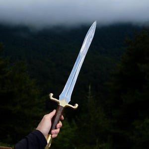 May include: A silver sword with a brown wooden handle and gold accents. The sword is held by a hand against a background of a misty forest.