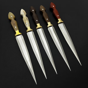 May include: Five handcrafted knives with polished steel blades and various handle materials. The handles include wood, bone, and horn, with brass bolsters. The knives are arranged diagonally against a black background, showcasing their sharp points.