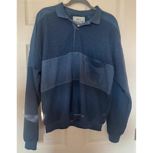 May include: A long-sleeve polo shirt in shades of blue, featuring a textured ribbed knit pattern on the upper chest, sleeves, and lower body. The shirt includes a solid blue horizontal mid-section with a chest pocket and a single button collar.
