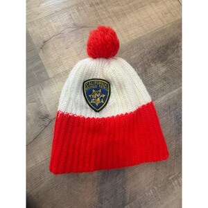 May include: A knitted winter hat with a red pom-pom and a two-tone design. The lower section is red, and the upper section is white. A patch with the words "California Highway Patrol" is sewn on the front.