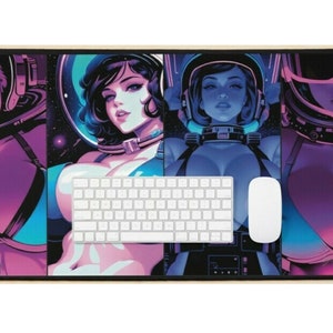 May include: A rectangular mouse mat with a striking illustration of four women in space helmets and suits. The artwork uses a palette of purple, blue, and pink. A white keyboard and mouse are placed on the mat.