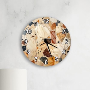 May include: Round wall clock with a terrazzo design in beige, brown, and black. The clock face features black numerals and hands. The clock is mounted on a white wall.