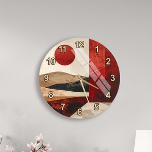 May include: A round wall clock with a modern design. The clock face features a landscape-inspired abstract art design in shades of red, brown, and beige. The clock hands are black, and the numbers are in a simple, easy-to-read font.