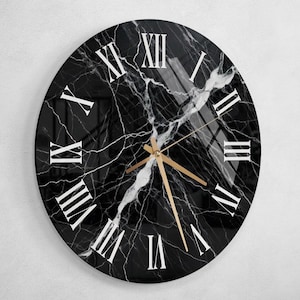 Puede incluir: Un reloj de mármol blanco y negro con números romanos. El reloj tiene manecillas doradas y un fondo negro.