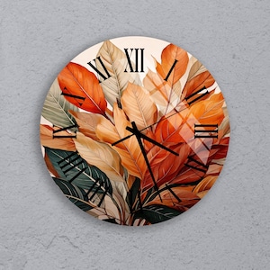 Puede incluir: Reloj de pared redondo con un diseño botánico de hojas naranjas, verdes y beige. La esfera del reloj tiene números romanos negros y manecillas negras. El reloj está montado en una pared gris.