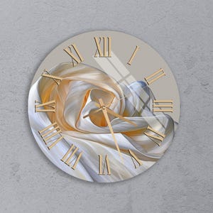May include: A round wall clock with a beige face and gold Roman numerals. The clock hands are gold. The center of the clock features an abstract design in shades of white, beige, and gold.