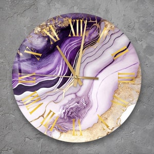 May include: Round wall clock with a purple and gold abstract design. The clock face features Roman numeral hour markers and gold hands.