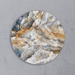 May include: Circular wall clock with a marble effect design in grey, white, and gold tones. The clock face has gold numerals and hands. The clock is mounted on a grey wall.