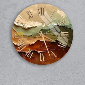 Peut inclure: Horloge murale ronde avec un motif de paysage abstrait dans des tons marron, vert et beige. Elle présente des chiffres romains et des aiguilles dorés. L'horloge est fixée sur un mur gris. Le diamètre de l'horloge est d'environ 30 cm.