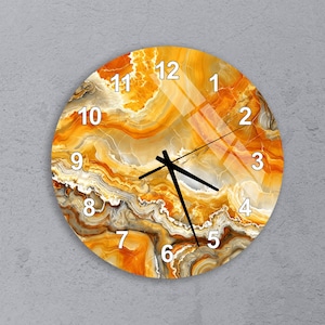 May include: Round wall clock with a marbled orange and yellow design. The clock face features black hands and white numerals. The clock is mounted on a gray wall.