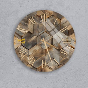 Peut inclure: Horloge murale ronde en bois avec un design géométrique. Le cadran est composé de différentes pièces de bois dans des tons bruns et gris. Des chiffres romains dorés indiquent les heures, et des aiguilles dorées indiquent l'heure. L'horloge est fixée sur un mur gris.