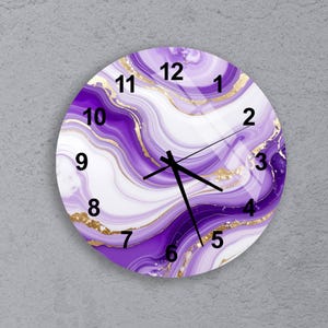 May include: Round wall clock with a marbled design in shades of purple, white, and gold. The clock face features black numerals and hands. The clock is a decorative item for home decor.