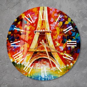May include: Round wall clock featuring a colorful impressionistic painting of the Eiffel Tower in Paris. The clock face has white Roman numerals and gold-colored hands. The artwork uses vibrant shades of red, orange, yellow, and blue.