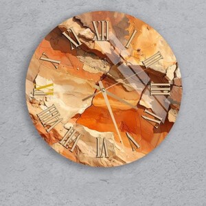 Könnte beinhalten: Runde Wanduhr mit einem strukturierten, erdigen Design in Orange-, Braun- und Beigetönen. Das Zifferblatt zeigt römische Ziffern und metallische Zeiger. Die Uhr ist an einer grauen Wand befestigt.