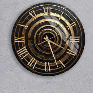 Puede incluir: Un reloj redondo negro y dorado con números romanos. La esfera presenta círculos concéntricos y manecillas doradas. El reloj está montado en una pared gris claro. El diseño del reloj es de estilo art déco.