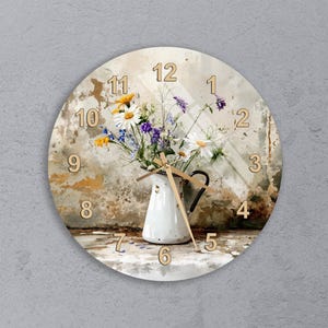 May include: Round wall clock featuring a watercolor design. The clock face has a distressed background with a white pitcher filled with colorful flowers. The clock hands are gold, and the numbers are in a wooden font.
