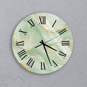 May include: Circular wall clock featuring a light green marble effect face with gold detailing. Black Roman numerals indicate the hours. The clock hands are black. A decorative item for a home or office.