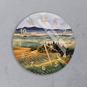 May include: Round wall clock featuring a scenic landscape painting of rolling hills, vineyards, and a farmhouse. The clock face has gold-colored numerals and hands. The background is a mix of green, yellow, and blue hues, creating a serene atmosphere.
