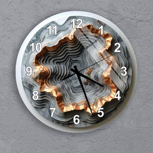 May include: A round wall clock with a white frame and a layered, topographic design in shades of gray and copper. The clock face features black hands and white numerals. The clock measures approximately 12 inches in diameter.