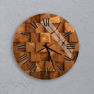 Puede incluir: Reloj de pared redondo de madera con un diseño único. La esfera del reloj está hecha de pequeños bloques de madera cuadrados en varios tonos de marrón. Los números romanos negros marcan las horas y las manecillas negras indican la hora. El reloj tiene una estética moderna y geométrica.