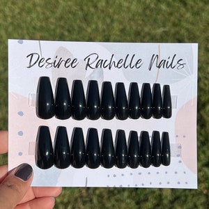 May include: A set of 10 black coffin-shaped press-on nails. The nails are arranged in two rows on a white card with the text "Desiree Rachelle Nails".