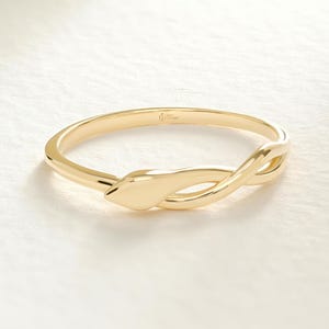 May include: A gold ring in the form of a snake. The ring has a smooth, polished surface and a coiled design, with the snake's head at one end. The ring is set against a soft, off-white background.