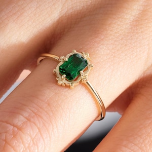 May include: A gold ring featuring a green gemstone set in an intricate, ornate design.