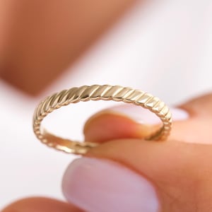 May include: A gold band ring with a twisted, rope-like design.