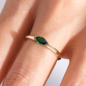 May include: A delicate gold ring with a marquise-shaped green gemstone.