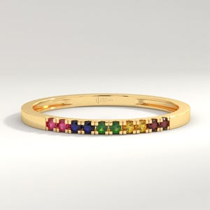 May include: A thin gold band ring with a rainbow of small gemstones set in the band. The gemstones are red, orange, yellow, green, blue, and purple.