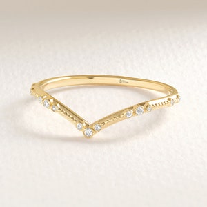 Peut inclure: Une bague en or jaune en forme de V ornée d'une série de petites pierres rondes et transparentes serties le long de l'anneau. L'anneau présente une texture perlée délicate entre les pierres, créant une silhouette en chevron polie.