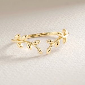 May include: A gold ring featuring a delicate design of two intertwined branches with leaves. The ring is open on one side, making it adjustable.