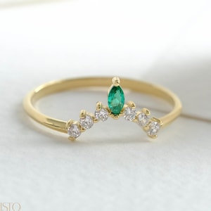 May include: A gold ring with a green emerald gemstone and small clear gemstones set in a curved band.
