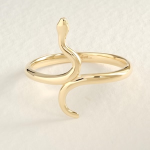 May include: A gold-colored ring in the shape of a snake. The snake's head is raised, and its body curves around the finger. The ring is made of a shiny, smooth metal.