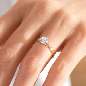 May include: A gold ring with a delicate, branch-like design. The ring features a round, clear gemstone in the center and smaller gemstones on the branches.