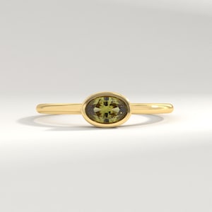 Puede incluir: Un anillo de oro con una piedra preciosa ovalada verde engastada en bisel.