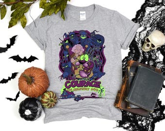 May include: A light gray t-shirt featuring a graphic from the animated series, Courage the Cowardly Dog. The design includes Courage, Muriel, and various spooky characters in shades of purple, green, and blue. The shirt has the show's logo.