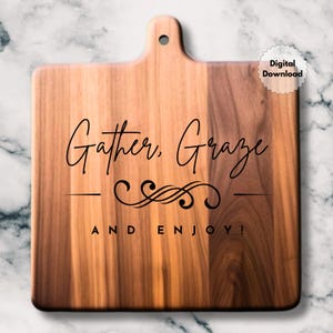 May include: Wooden chopping board with a handle, featuring the words "Gather, Graze, and Enjoy!" in black script. The board has a light and dark brown wood grain. A digital download sticker is in the upper right corner.